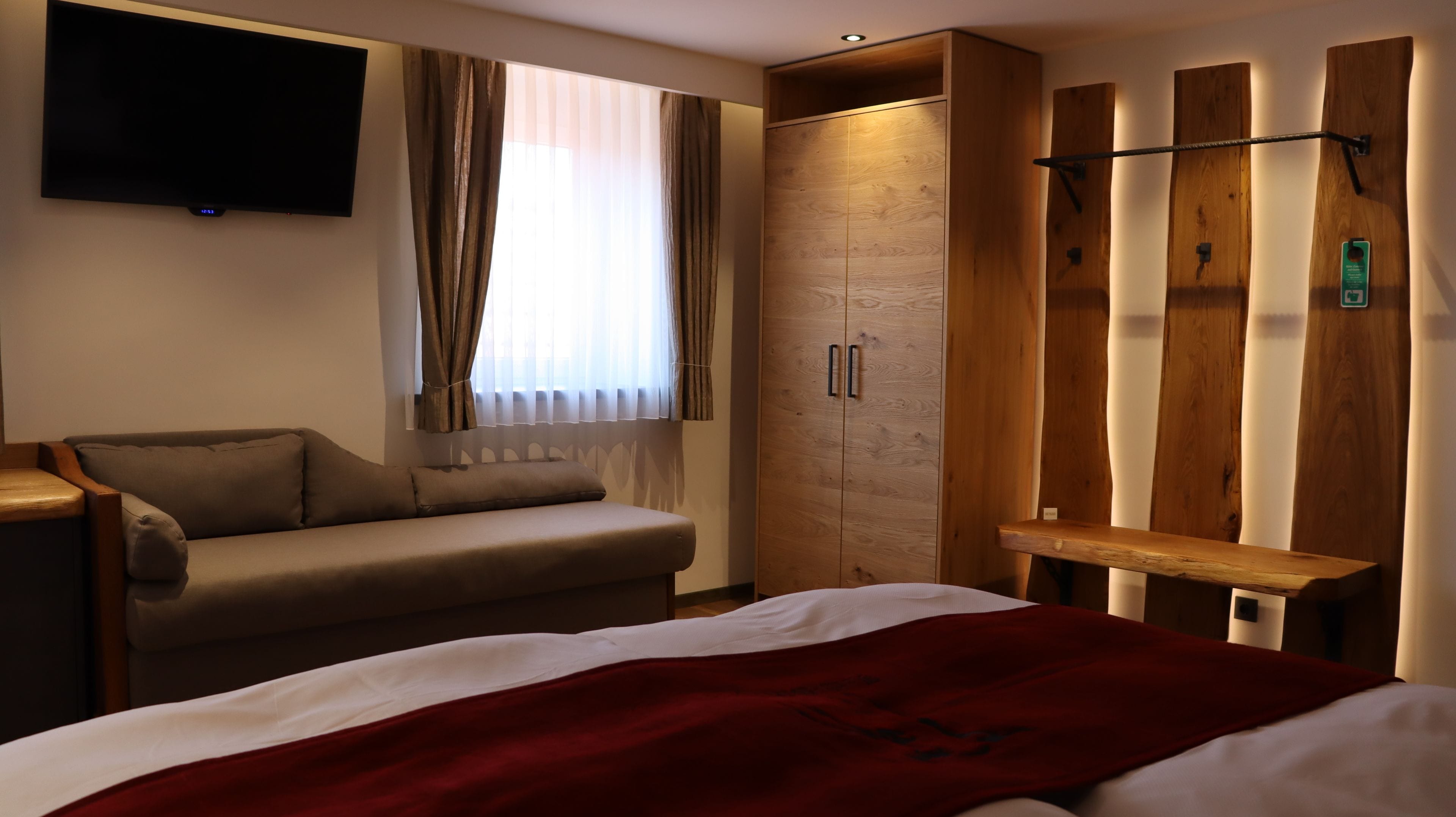 Una habitació d'hotel amb un llit, un sofà, un televisor penjat a la paret i un armari de fusta amb una panxa.