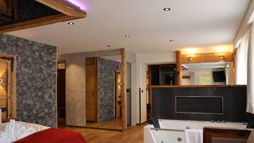 Habitación de hotel moderna con suelo de madera, pared de acento de piedra, espejo grande, bañera y colcha roja.