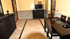 Uma cozinha moderna com bancada de madeira escura, televisão integrada e área de refeições com uma mesa grande e cadeiras.