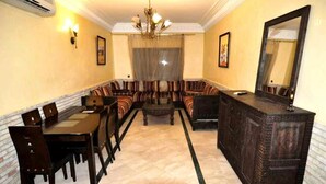Uma sala de estar ampla com um amplo sofá, uma mesa de jantar com cadeiras, um armário de madeira escura e um espelho grande.