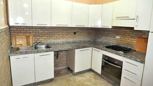 Cozinha com armários brancos, bancada de granito, pia, fogão e lava-louças.