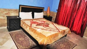 Ein ordentlich eingerichtetes Schlafzimmer mit einem Bett, zwei Nachttischen, einer Lampe und einem roten Vorhang.
