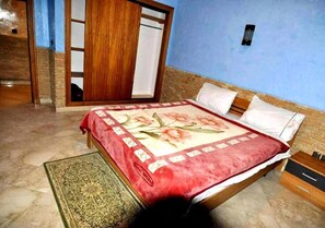 A bedroom with a bed, a wooden wardrobe, a small table, and a nightstand.