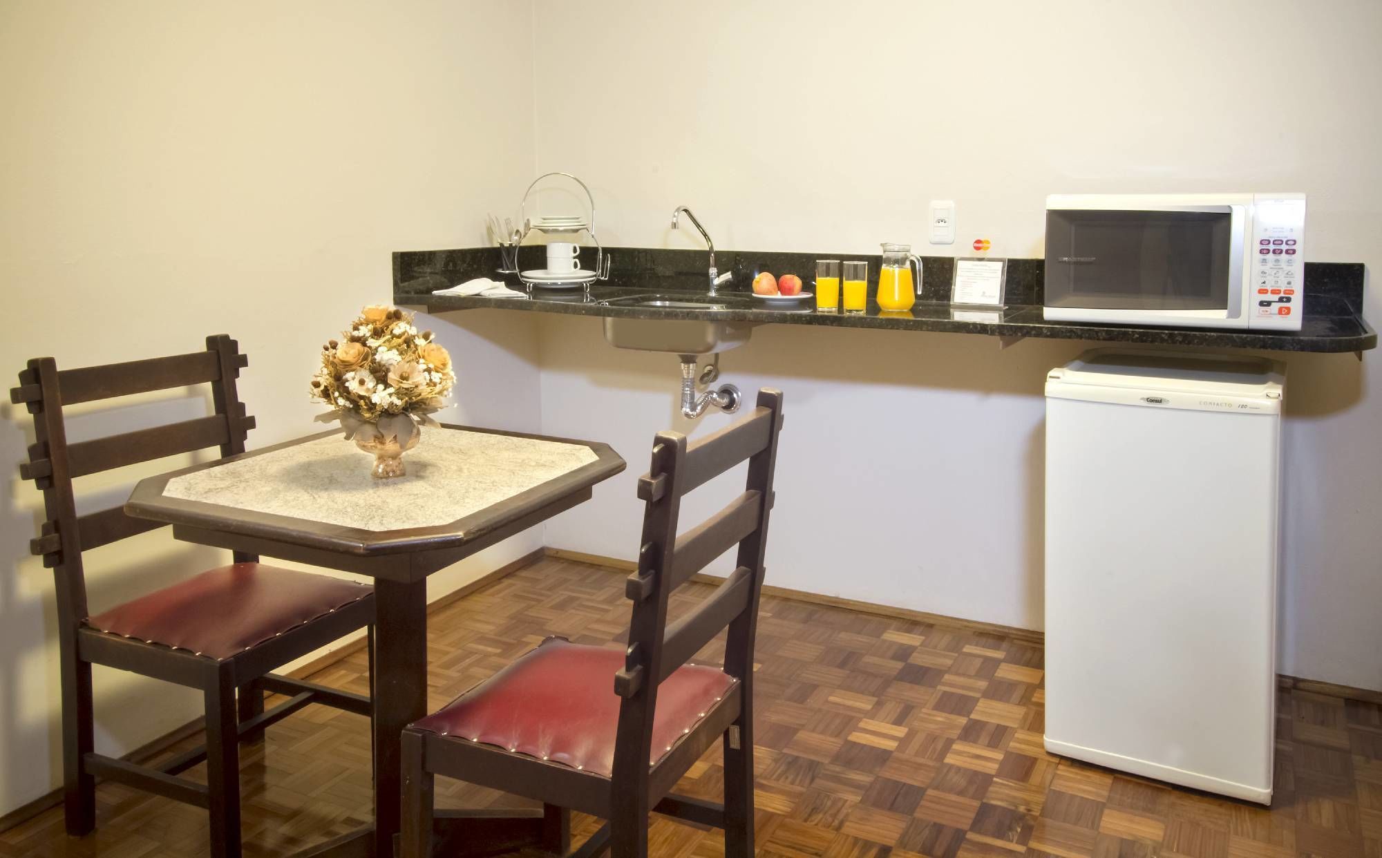 A compact kitchen with a dining table, chairs, a refrigerator, a microwave, and a sink.