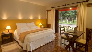 A hotel room with a bed, bedside lamps, a laptop on a table, and a view of a park through a window.
