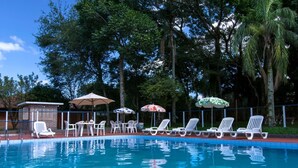 A swimming pool with white lounge chairs and umbrellas, surrounded by trees.