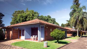 A single-story house with a tiled roof, a small porch with two chairs, and a well-maintained lawn.