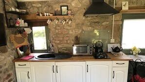 Una cocina con pared de piedra, armarios blancos, un lavabo negro, un tostador y una tetera.