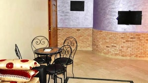 Una habitació amb una llar de foc de maó, una taula rodona amb caires i una televisió penjada a la paret.
