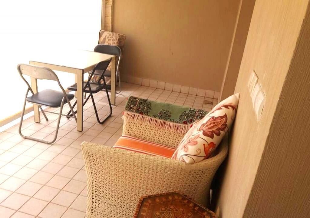 Un petit espace patio clos, aménagé avec un canapé en osier, une table à manger avec des chaises et un coussin à motifs.