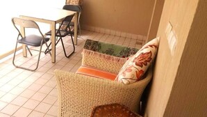 En lille, lukket patio med en fletsofa, et spisebord med stole og en pude med mønster.