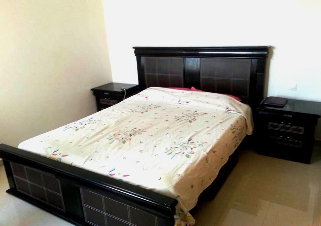 Un lit avec une couvre-lit à motifs floraux, une tête de lit sombre et deux tables de chevet dotées de tiroirs.