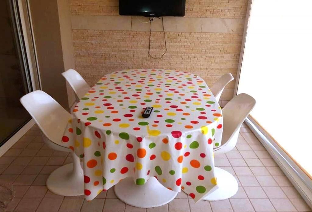 A round table with a polka dot tablecloth, surrounded by white chairs, in a room with a brick wall and a television mounted above.