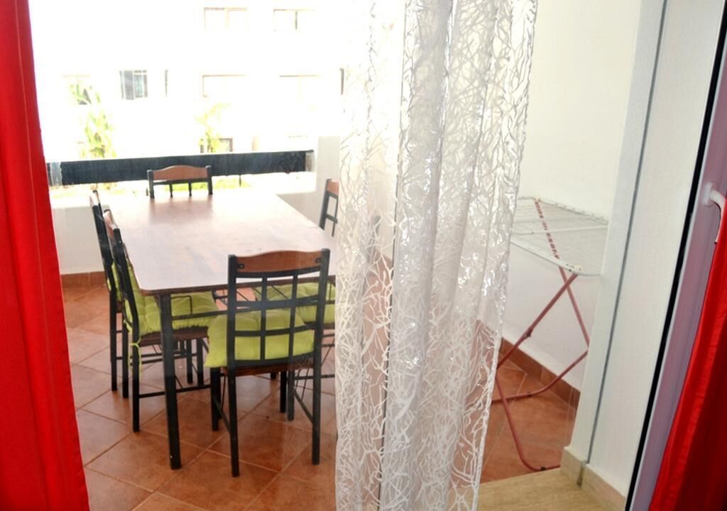 Un coin repas avec une table et des chaises, un rideau blanc et une vue sur l’extérieur.