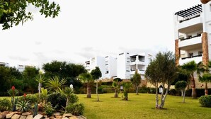 A residential area with modern white buildings, a well-maintained grassy lawn, and various trees and shrubs. - Residence Playa del Pacha Mdiq 3407 (Mdiq)