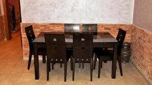 Comedor con mesa rectangular y seis sillas, pared decorativa de ladrillo y suelo de baldosas.
