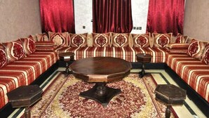 Una habitación con un amplio sofá ricamente decorado, una mesa redonda central y un tapete estampado.