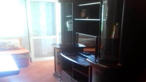 Ein Zimmer mit einem dunklen Holzschrank, einer Glastür zum Außenbereich und einem Fliesenboden.