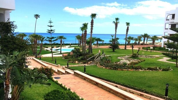 A resort with a pool, palm trees, and a view of the ocean.