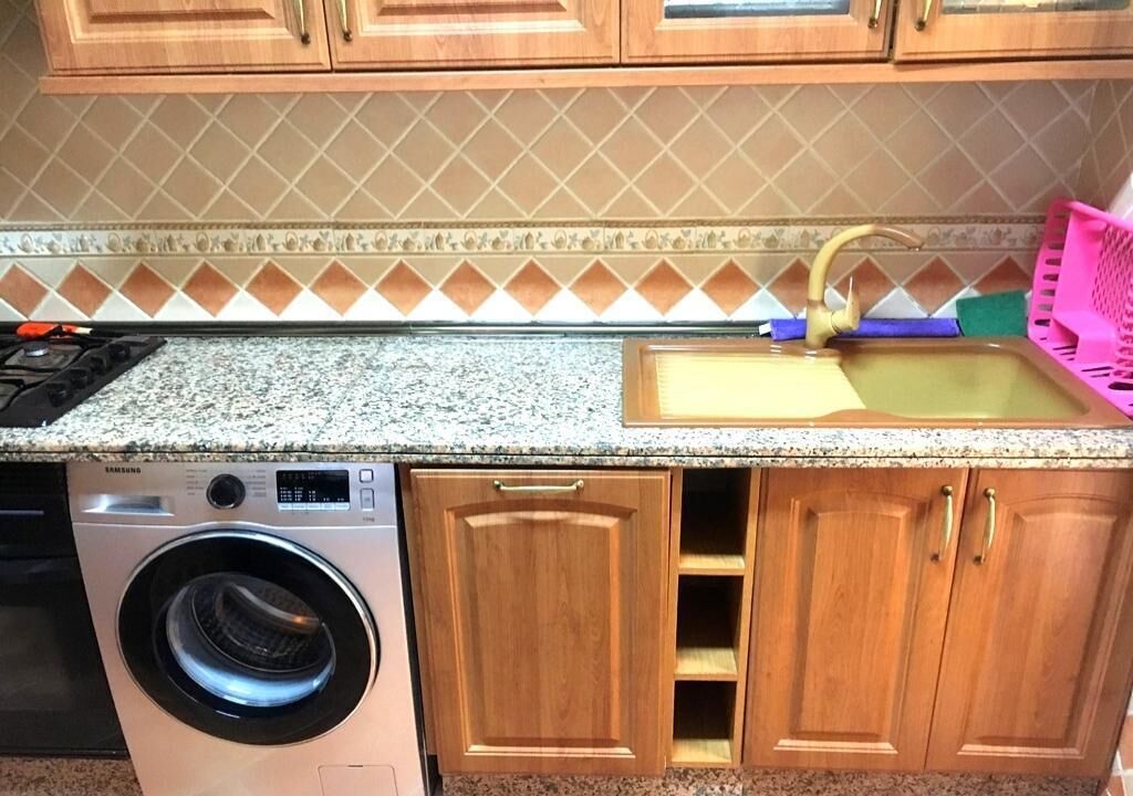 A kitchen with wooden cabinets, a washing machine, and a sink with a pink dish rack.
