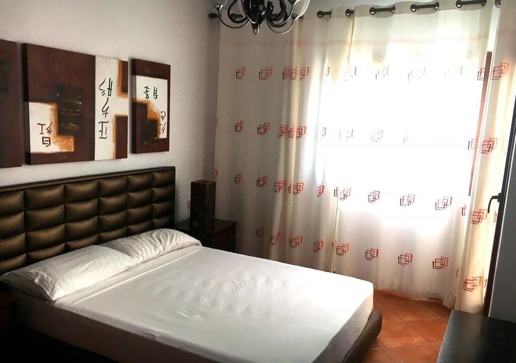 Une chambre à coucher comprenant un lit, une tête de lit, une table de chevet et un rideau à motifs.