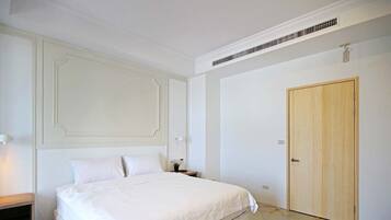 Un dormitorio con una cama grande, una puerta de madera y una mesita de noche con lámpara.