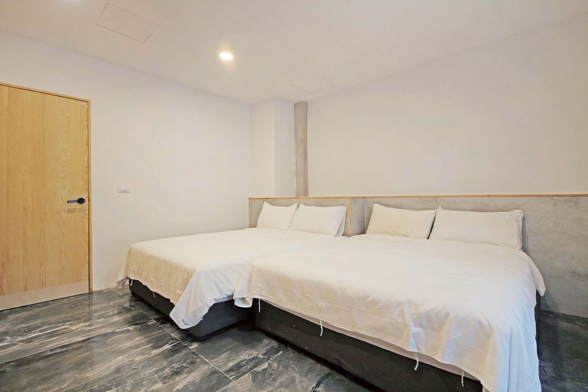 A double bed with a wooden headboard in a room with a marble floor and a wooden door.