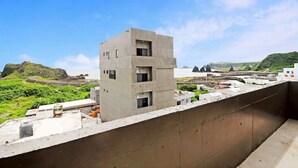 A modern concrete building with multiple windows, surrounded by greenery and a coastal landscape. - House16 (Lyudao)