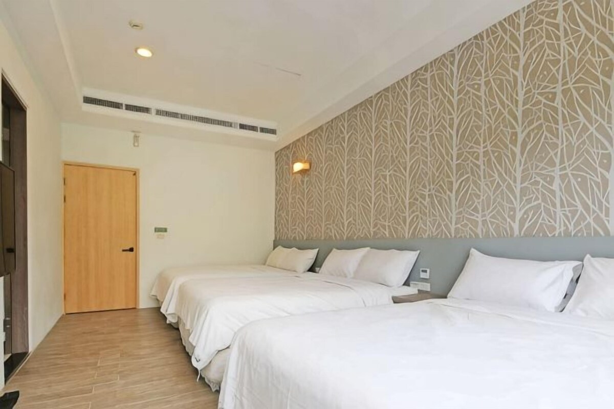 A hotel room with two beds, a patterned wall, a door, and a ceiling vent.