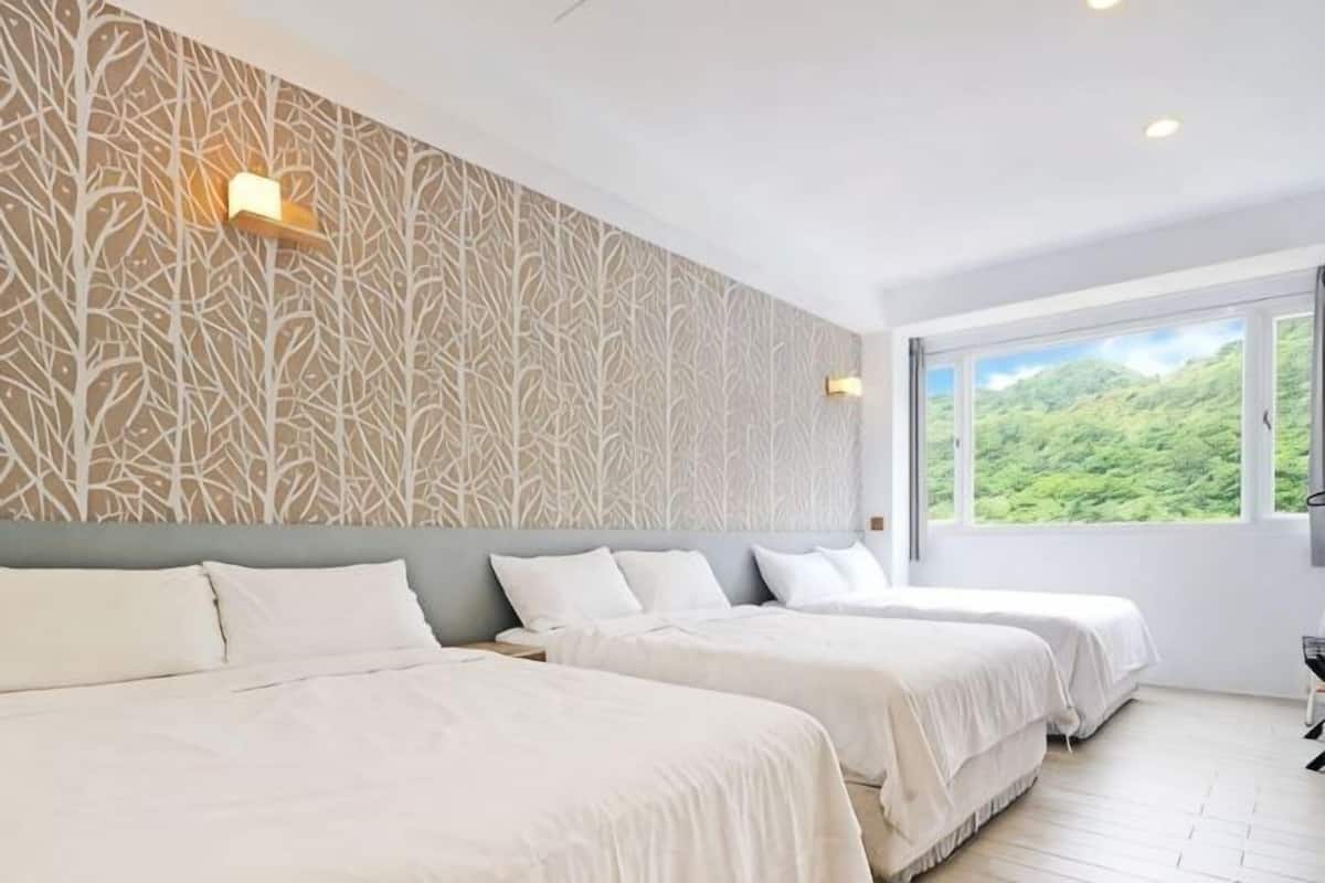 A hotel room with two beds, a patterned wall, and a large window with a view of greenery.