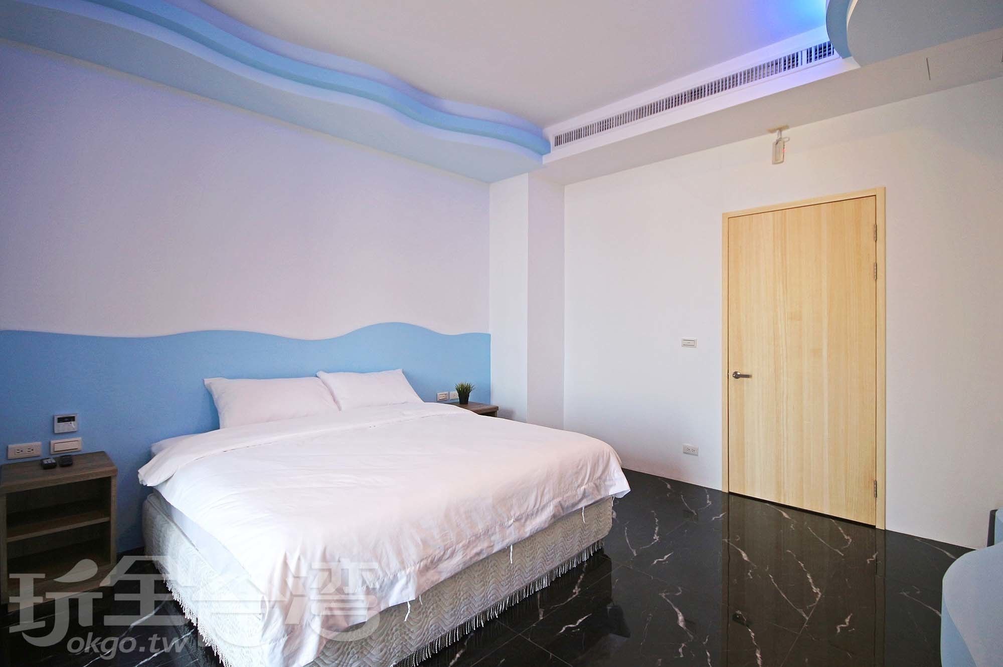A bedroom with a bed, a nightstand, a wooden door, and a wall with a blue and white design.