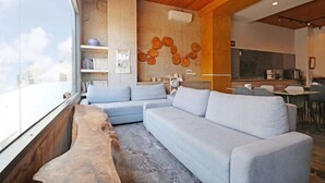 A modern living room with a large sofa, a coffee table, and a dining area with a kitchen in the background. - House16 (Lyudao)
