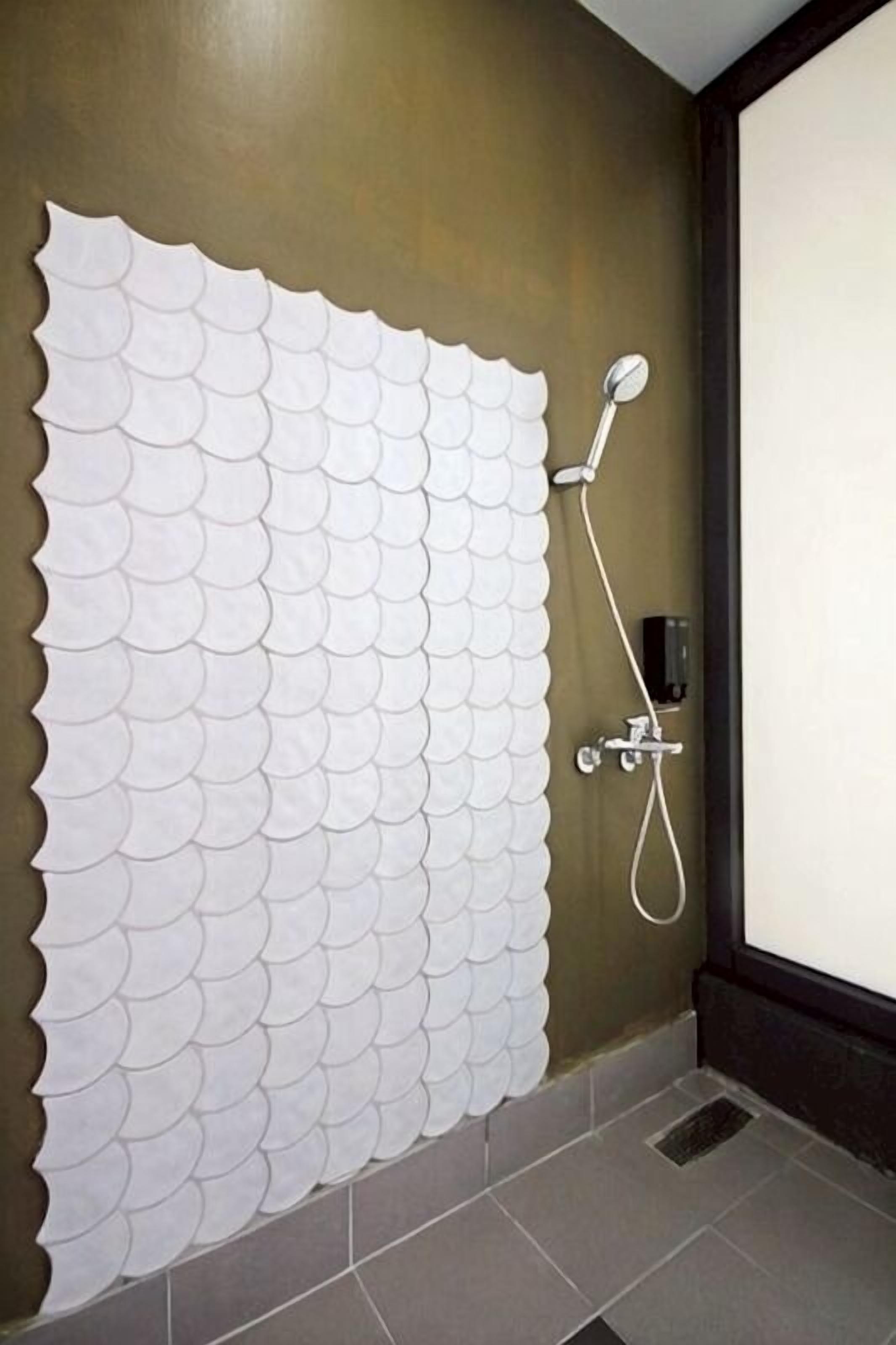 A bathroom with a tiled floor, a shower with a handheld showerhead, and a wall with a white, scalloped tile design.
