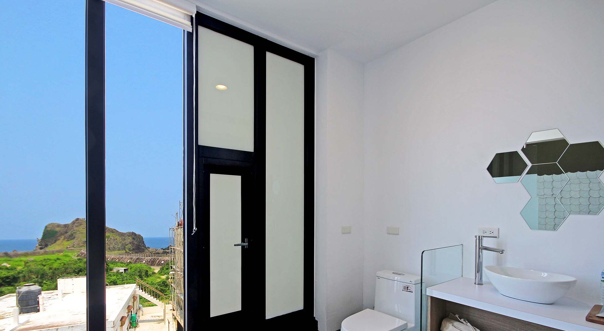 A modern bathroom with a large window, a white sink, and a toilet.