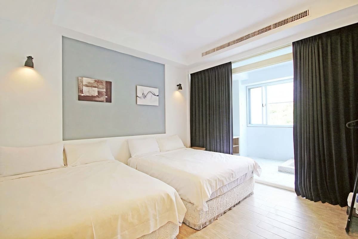 A hotel room with two beds, a large window with curtains, and artwork on the wall.