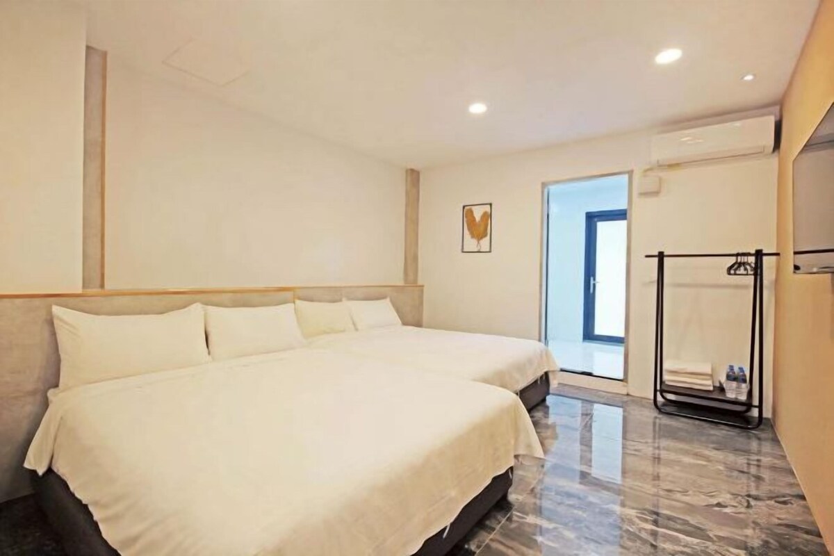 A modern hotel room with two beds, a marble floor, a coat rack, and a view of the outside.