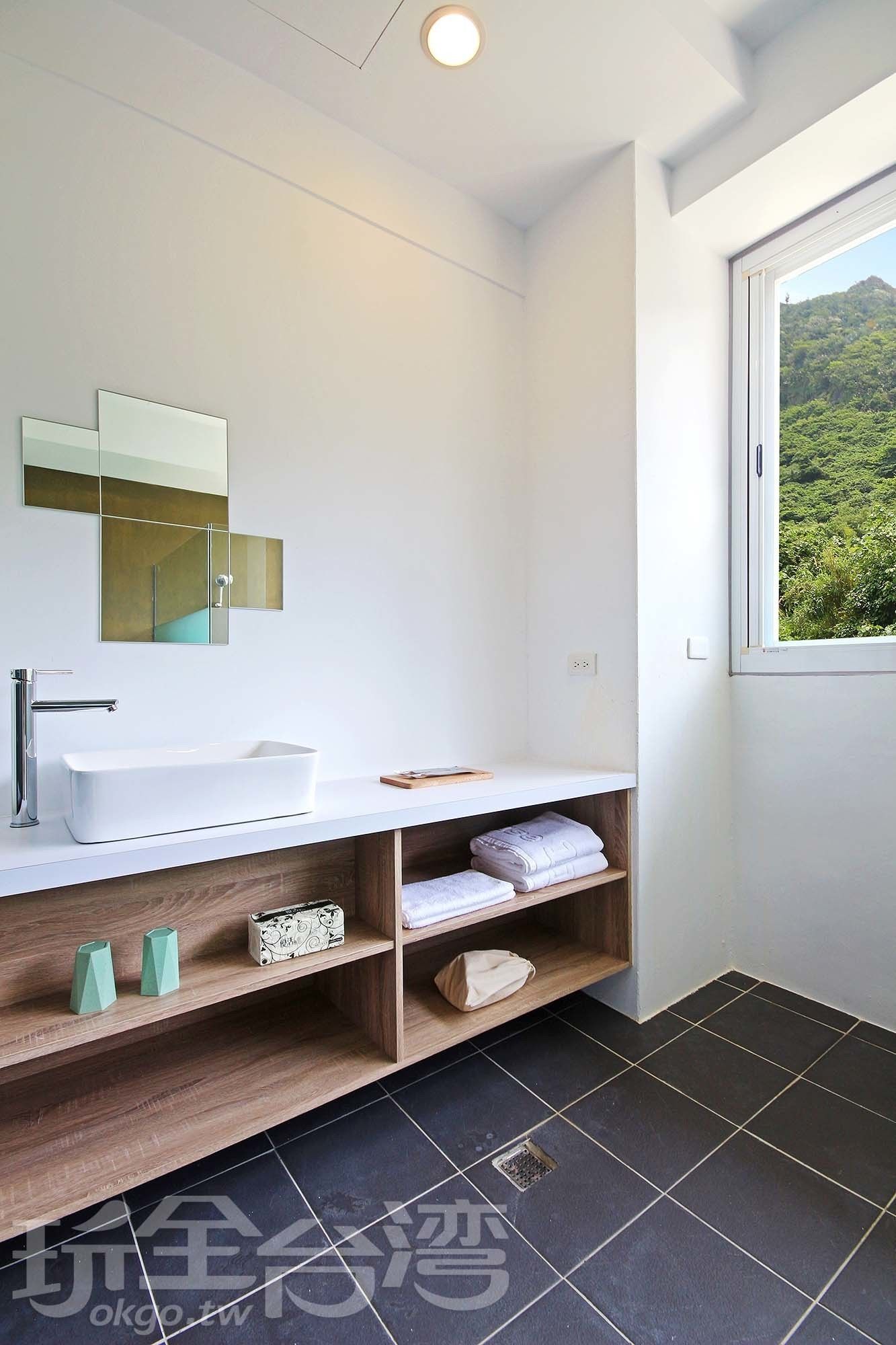 Une salle de bain moderne avec un lavabo blanc, un miroir et une fenêtre donnant sur un paysage verdoyant.