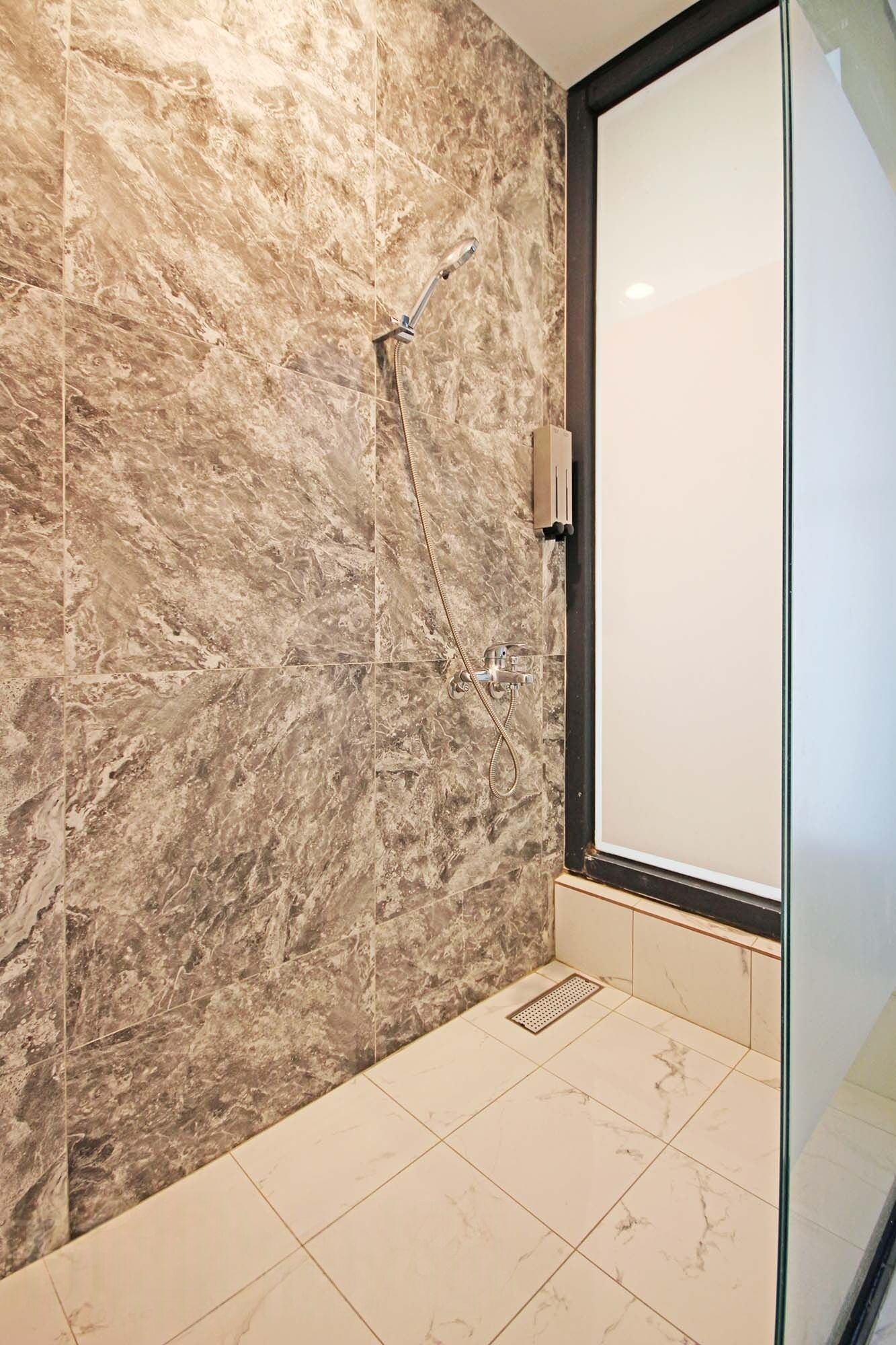 A modern bathroom with marble walls and a glass shower enclosure.