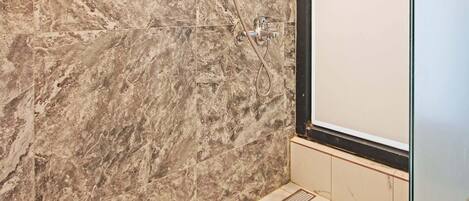 A modern bathroom with marble walls and a glass shower enclosure.