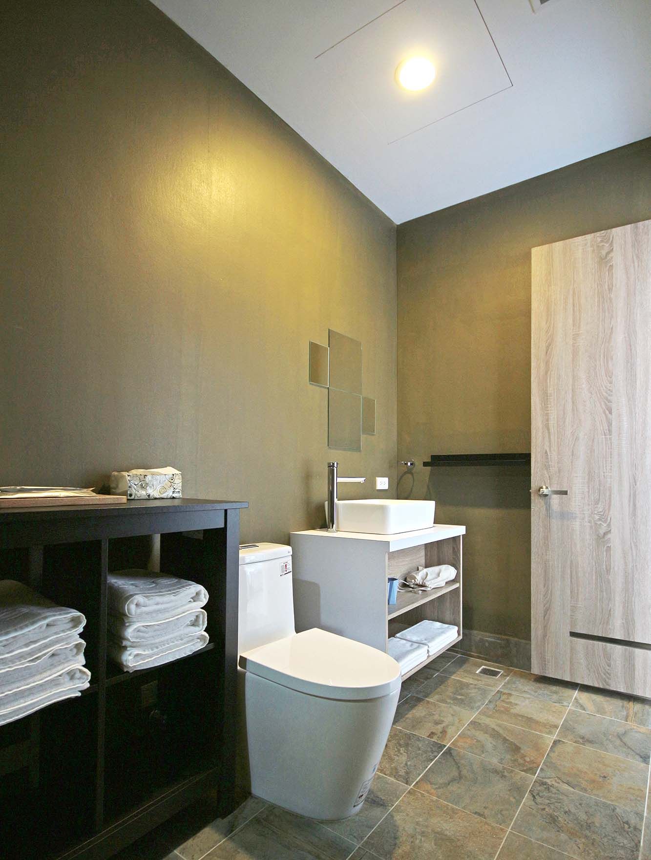 Een moderne badkamer met toilet, wastafel en een badkamermeubel. Er is een handdoekrek en een kast met opgevouwen handdoeken.