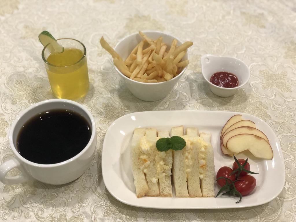 A table with a white plate of sliced bread, cherry tomatoes, and apple slices, a bowl of fries, a cup of coffee, and a glass of tea with a mint garnish.