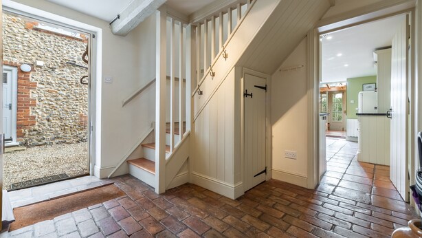 A staircase with white railings leading to a door, a stone wall outside, and a kitchen area visible through an open door. - Arch Cottage, Burnham Market, Norfolk (Burnham Market)