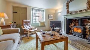 A cozy living room with a leather armchair, a wooden coffee table with wine glasses, a fireplace, and a television. - Arch Cottage, Burnham Market, Norfolk (Burnham Market)