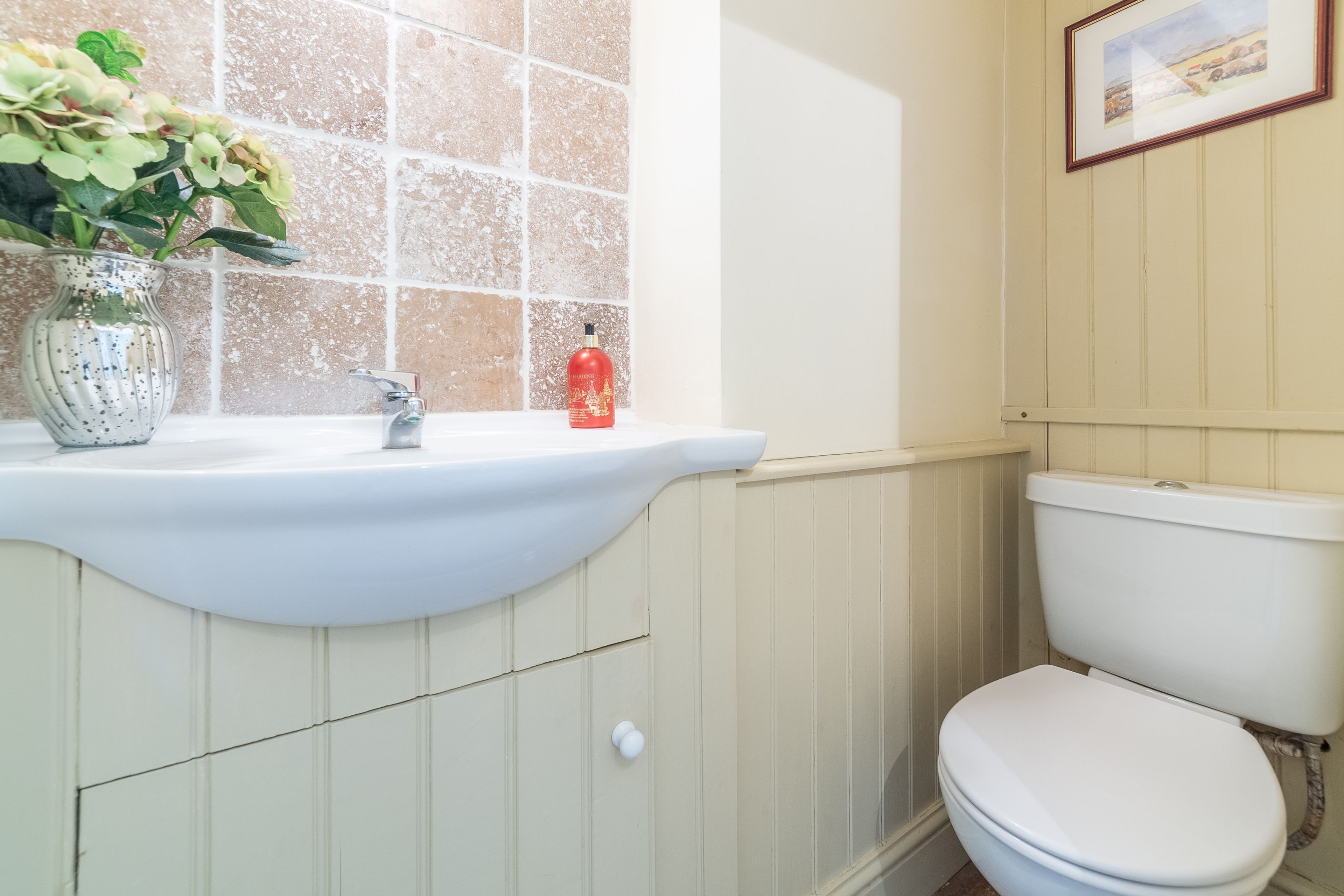 Ein Badezimmer mit Waschbecken, Blumen in einer Vase, einer roten Flasche und einer Toilette.