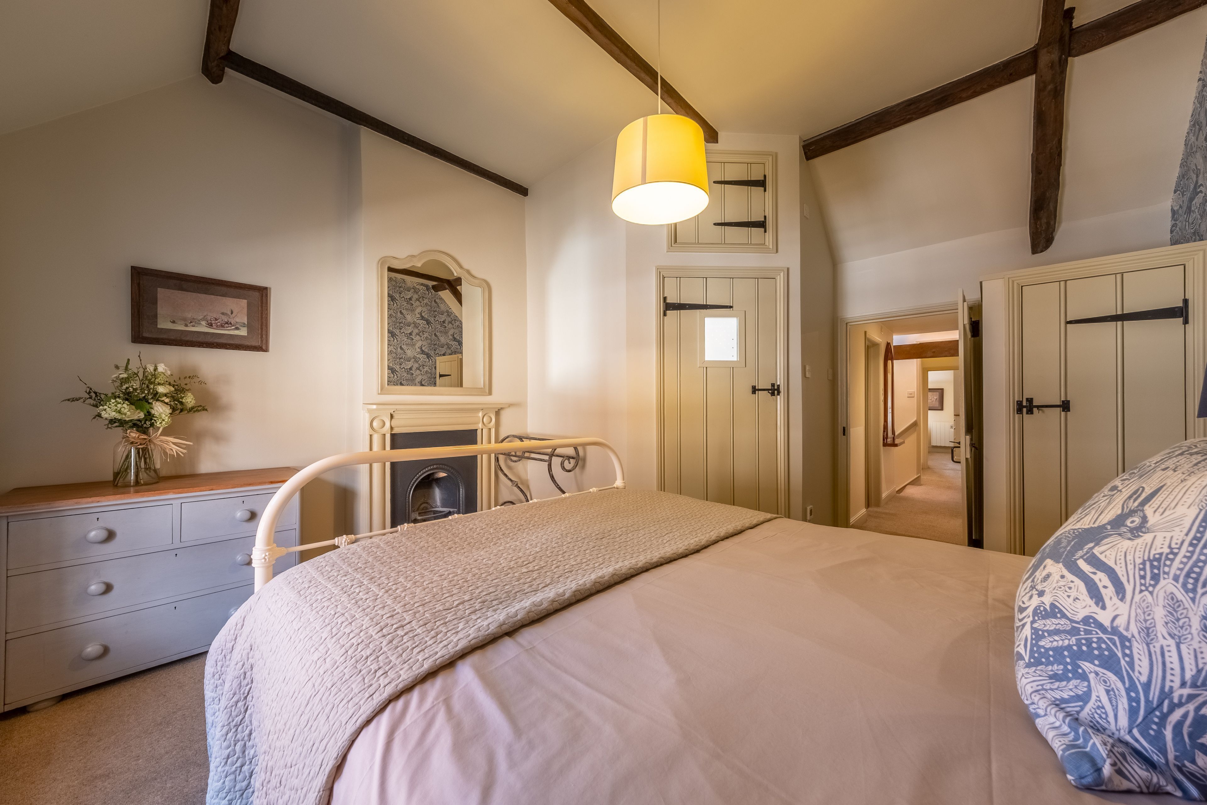 Ein Schlafzimmer mit Bett, Nachttisch, Schminktisch und Spiegel. Eine Tür führt in einen anderen Raum.