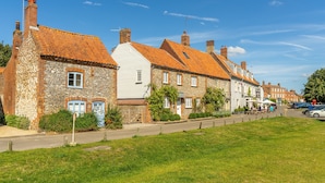 A row of traditional stone houses with red-tiled roofs, a grassy front yard, and a clear blue sky. - Arch Cottage, Burnham Market, Norfolk (Burnham Market)