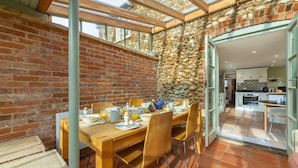 A dining area with a brick wall, wooden table, and chairs. - Arch Cottage, Burnham Market, Norfolk (Burnham Market)