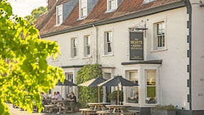 A traditional building with a sign reading "The Hoste Arms." It features outdoor seating with tables and umbrellas, and a well-maintained garden area. - Arch Cottage, Burnham Market, Norfolk (Burnham Market)