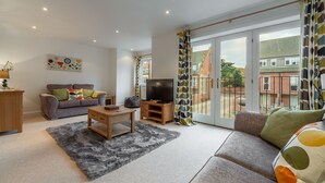 A modern living room with a sofa, coffee table, TV, and a view of a balcony. - The Moorings, Wells-next-the-Sea, Norfolk (Wells-next-the-Sea)