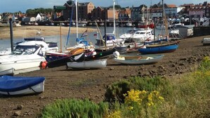 A harbor with various boats docked along the shore, surrounded by buildings and a sandy beach. - The Moorings, Wells-next-the-Sea, Norfolk (Wells-next-the-Sea)